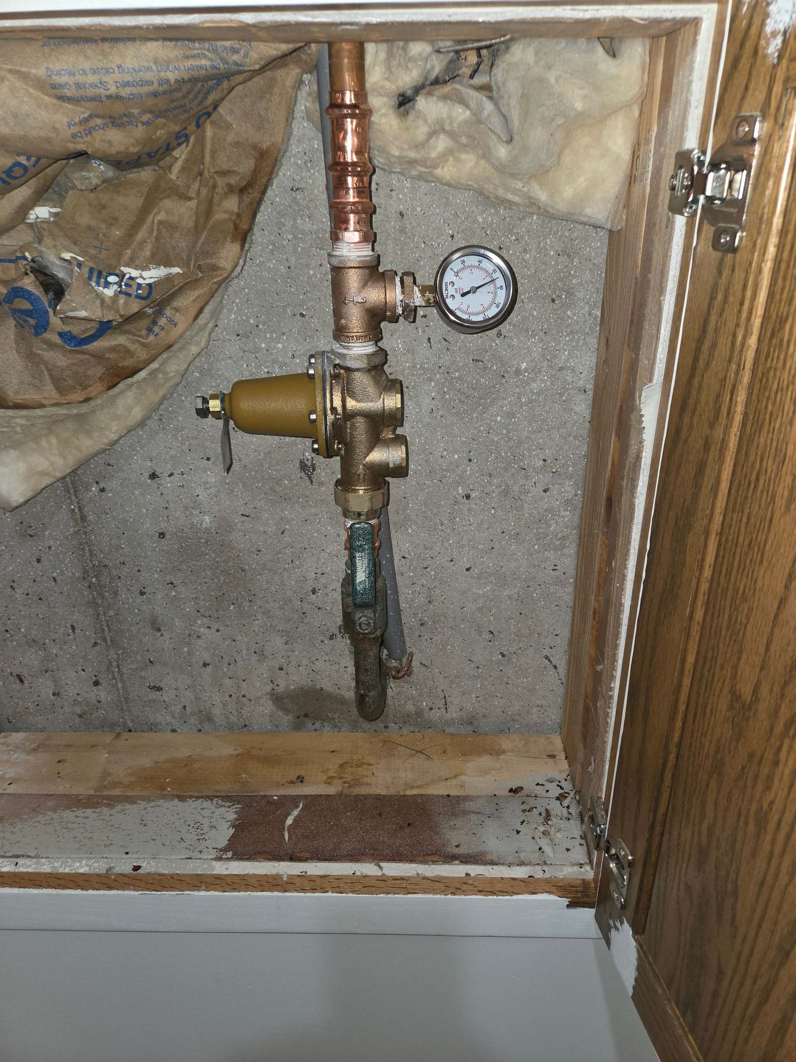 Brass pressure reducing valve and gauge on copper pipe, seen through an opened cabinet access panel