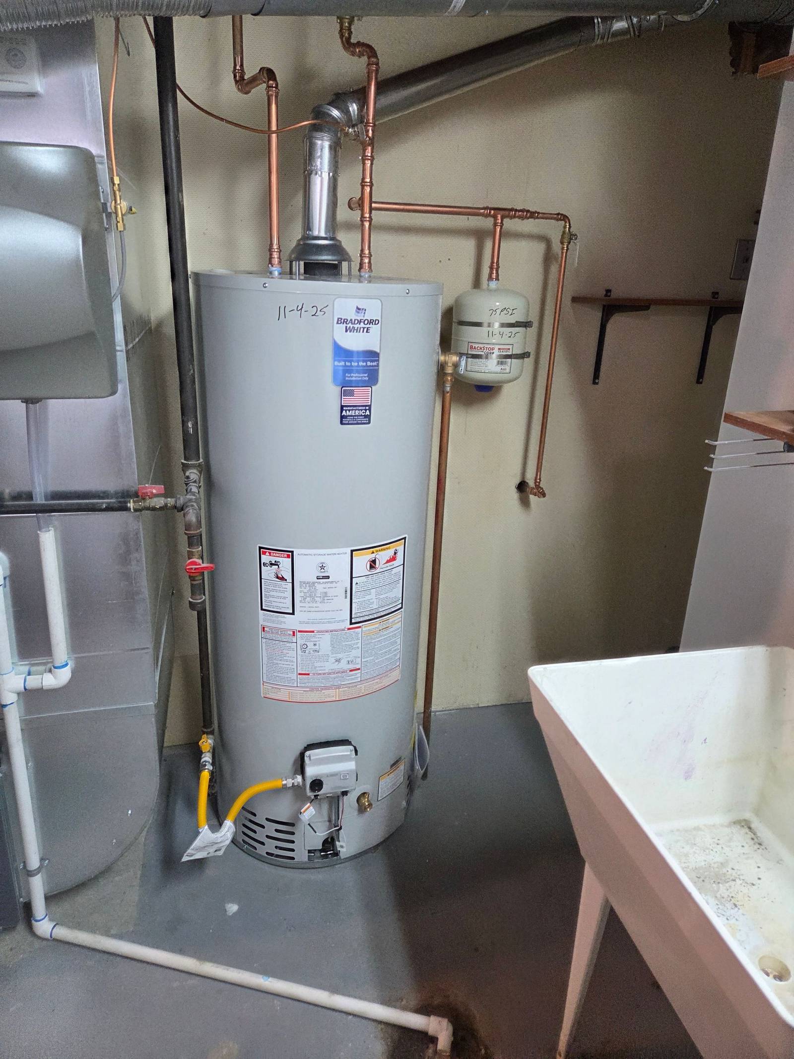 Bradford White tank water heater with copper piping, gas line and expansion tank installed in a finished basement utility room