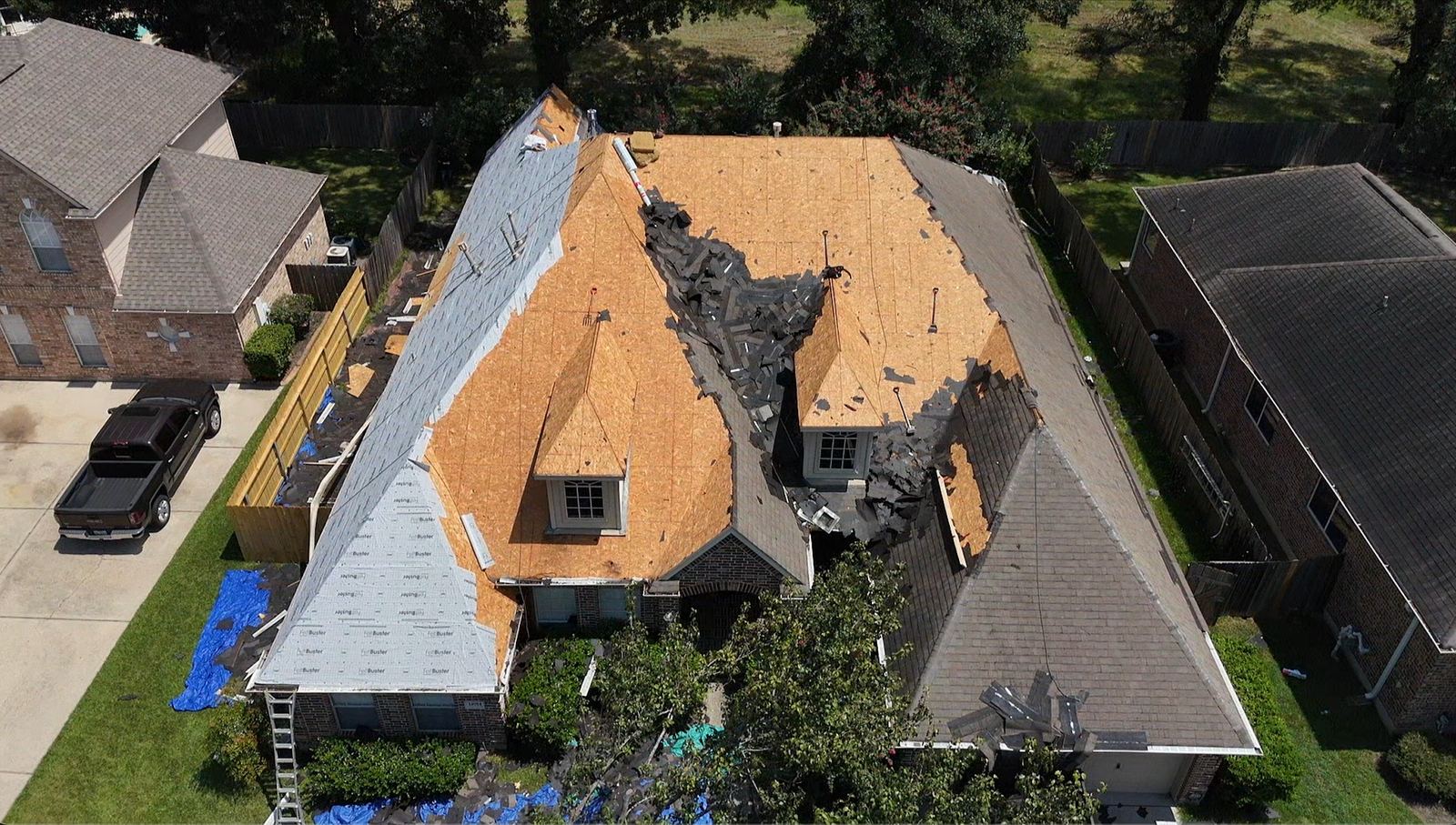 Aerial view of a house mid-reroof, with old shingles torn off in patches, bare decking exposed and a ladder against the eave