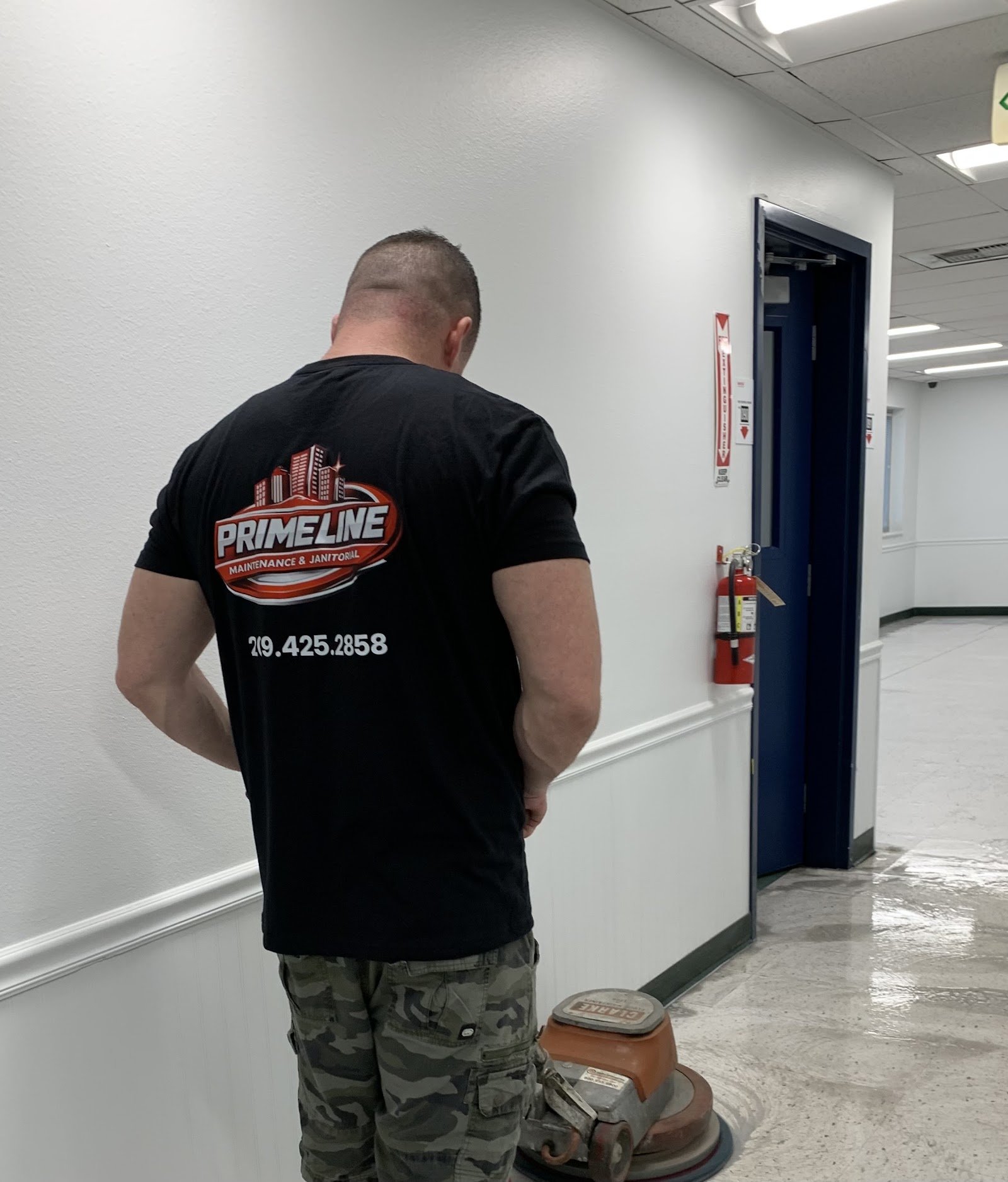 Man in a Primeline shirt running a floor buffer along a white hallway with a wet, polished floor