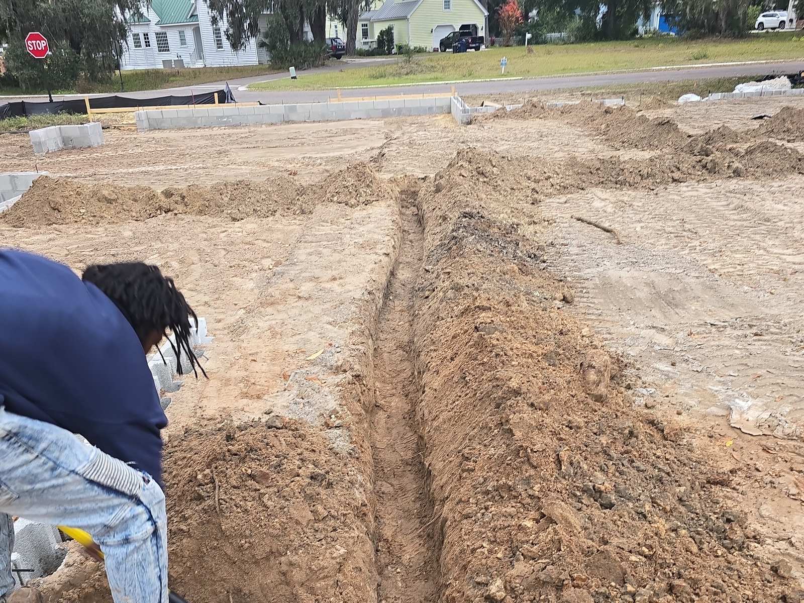 A worker digs a long trench across a cleared building lot