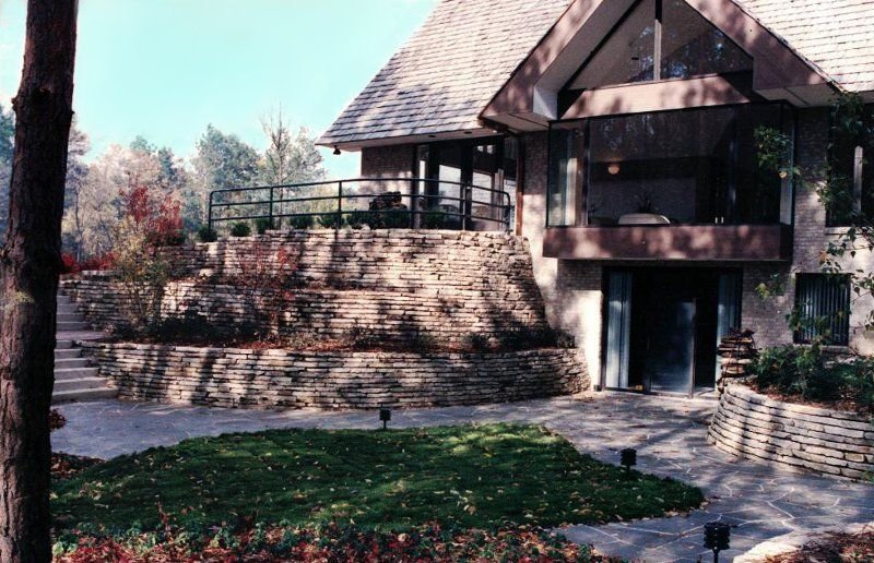 Tiered natural stone retaining walls beside a flagstone patio and a modern house with large windows
