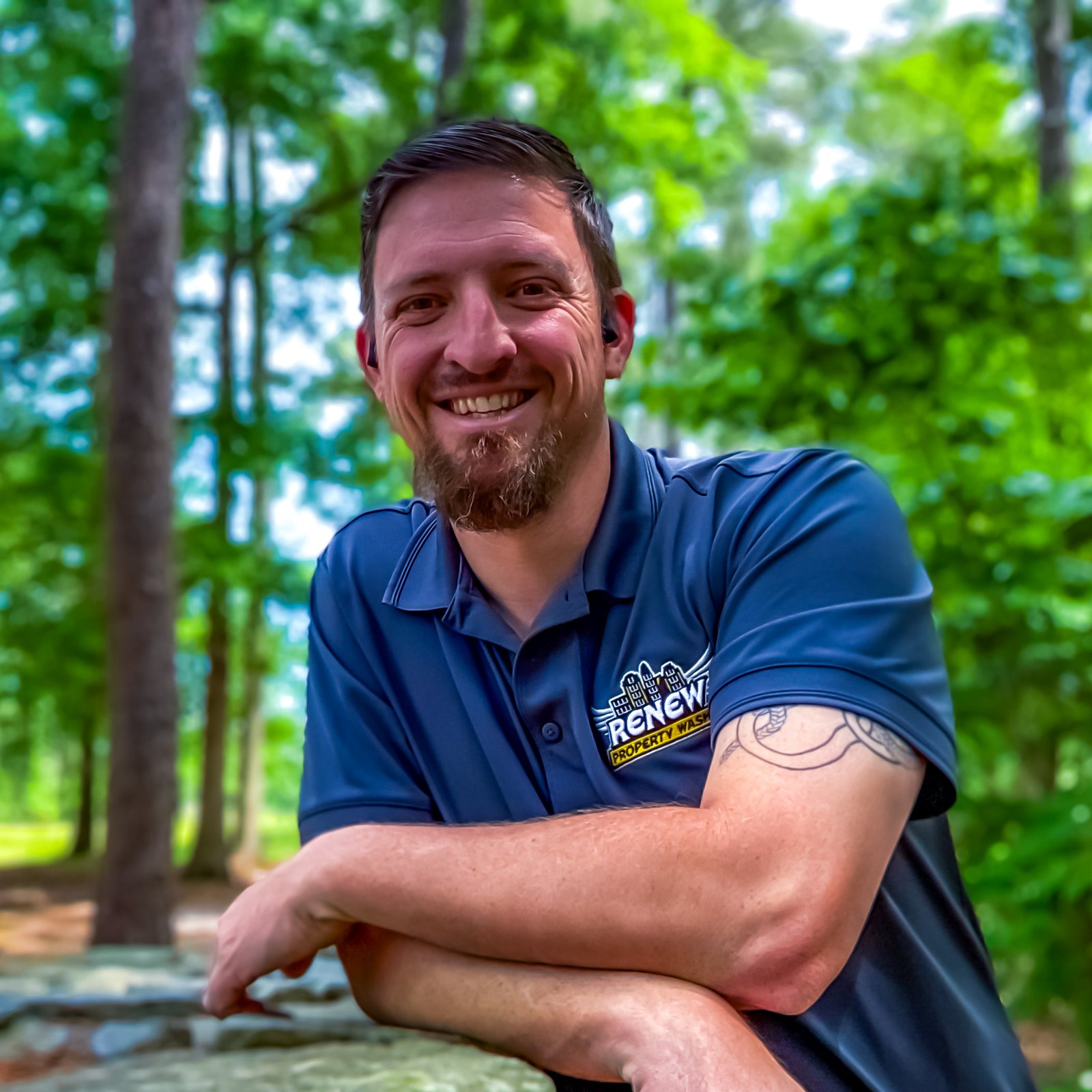 Smiling owner of Renew Property Wash in a branded navy polo, standing outdoors by trees