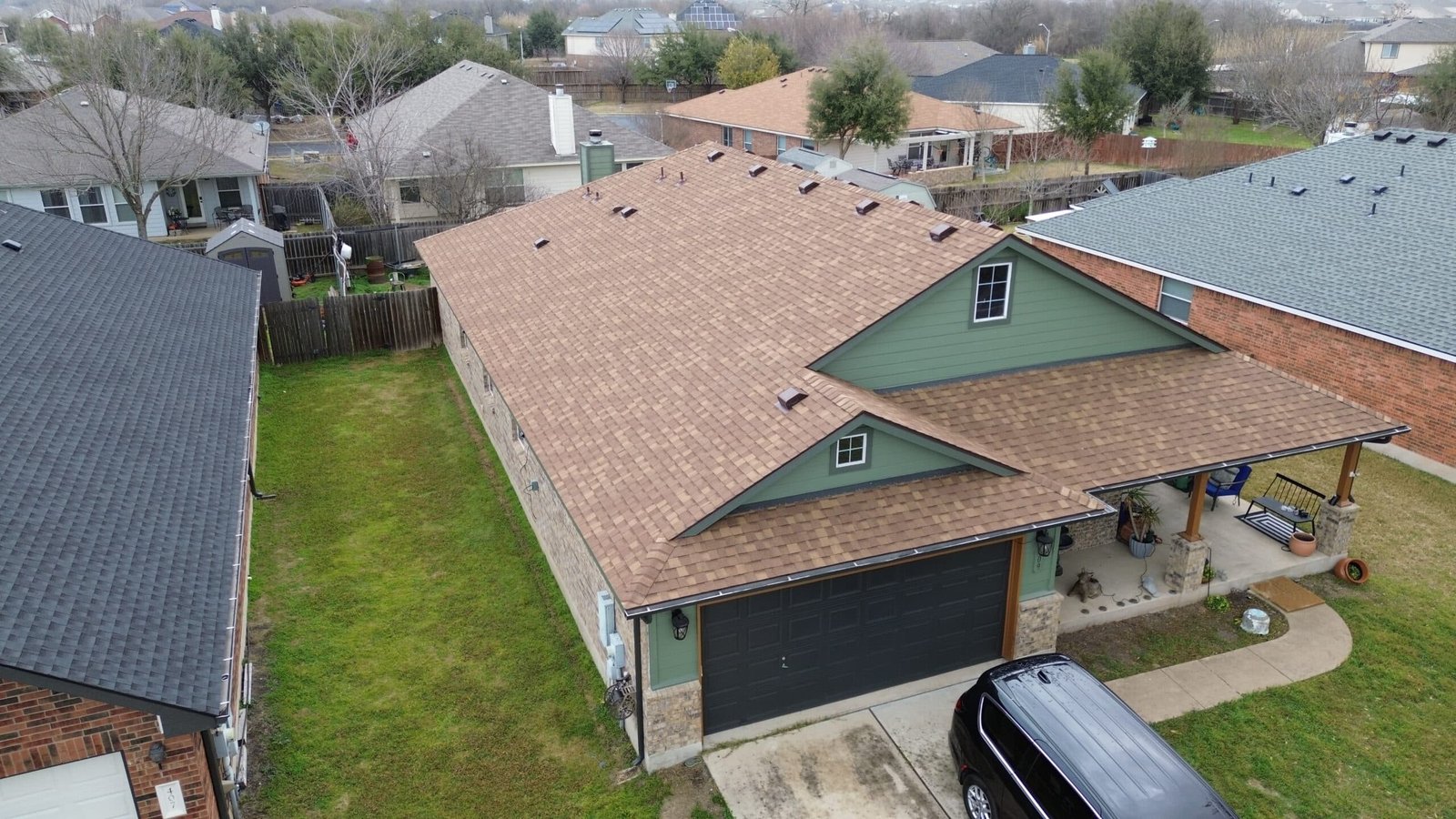 Aerial view of a brick house with a new brown asphalt shingle roof, green gables and a covered patio