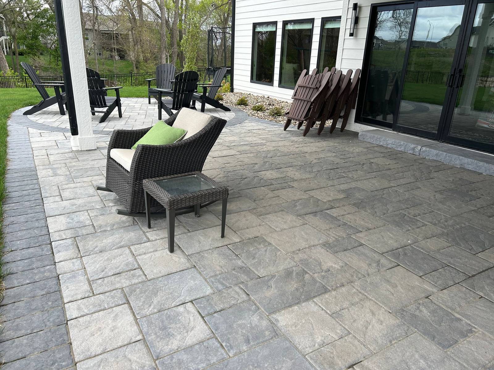 Large gray paver patio beside a house with sliding glass doors, patio chairs and a paver border