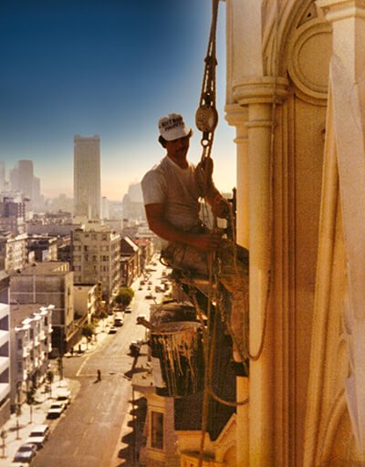 Mark Solomon in rope rigging high on the face of a church above a city street