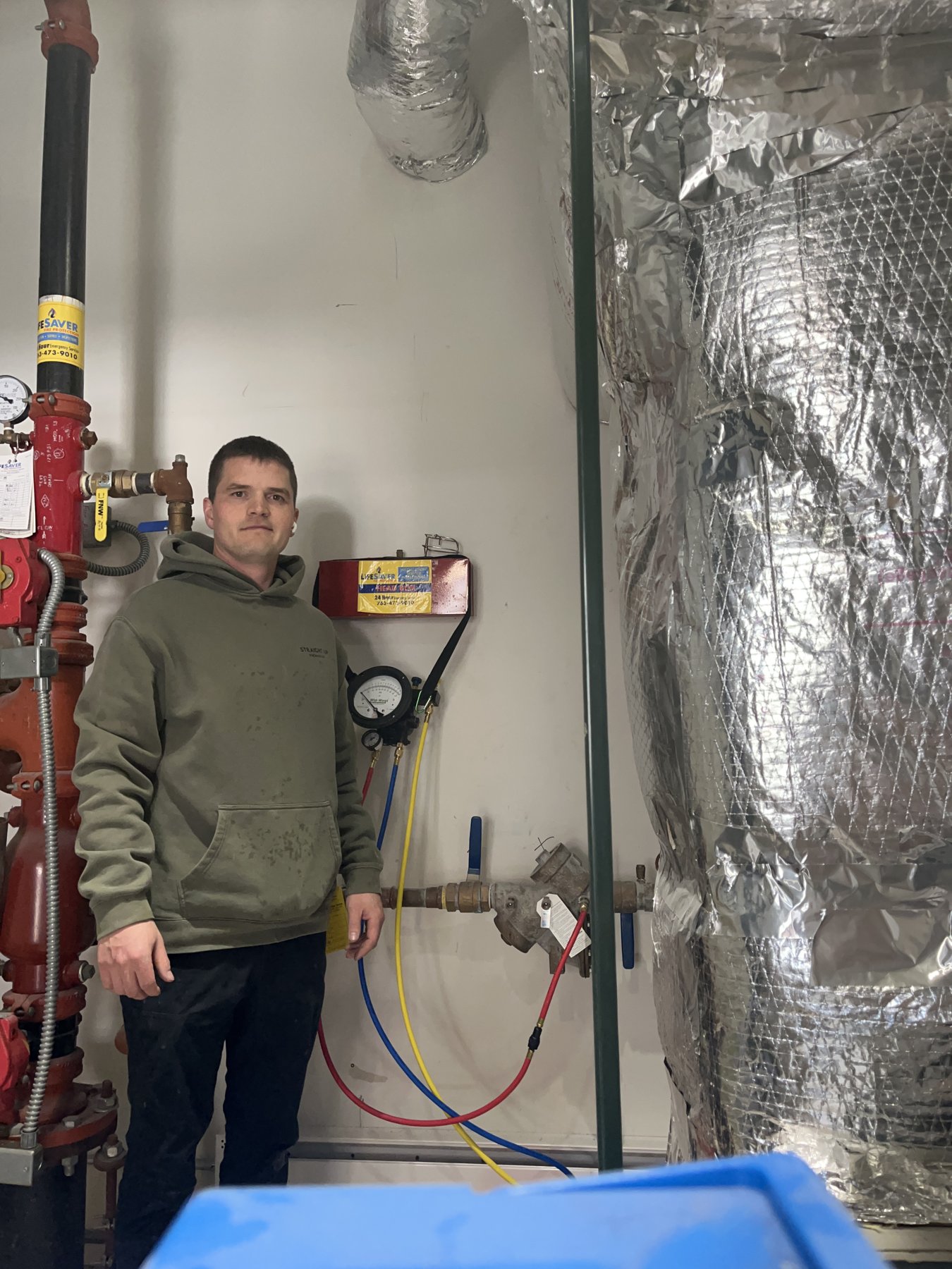 Michael Redinger stands beside a backflow preventer and test gauge in a mechanical room