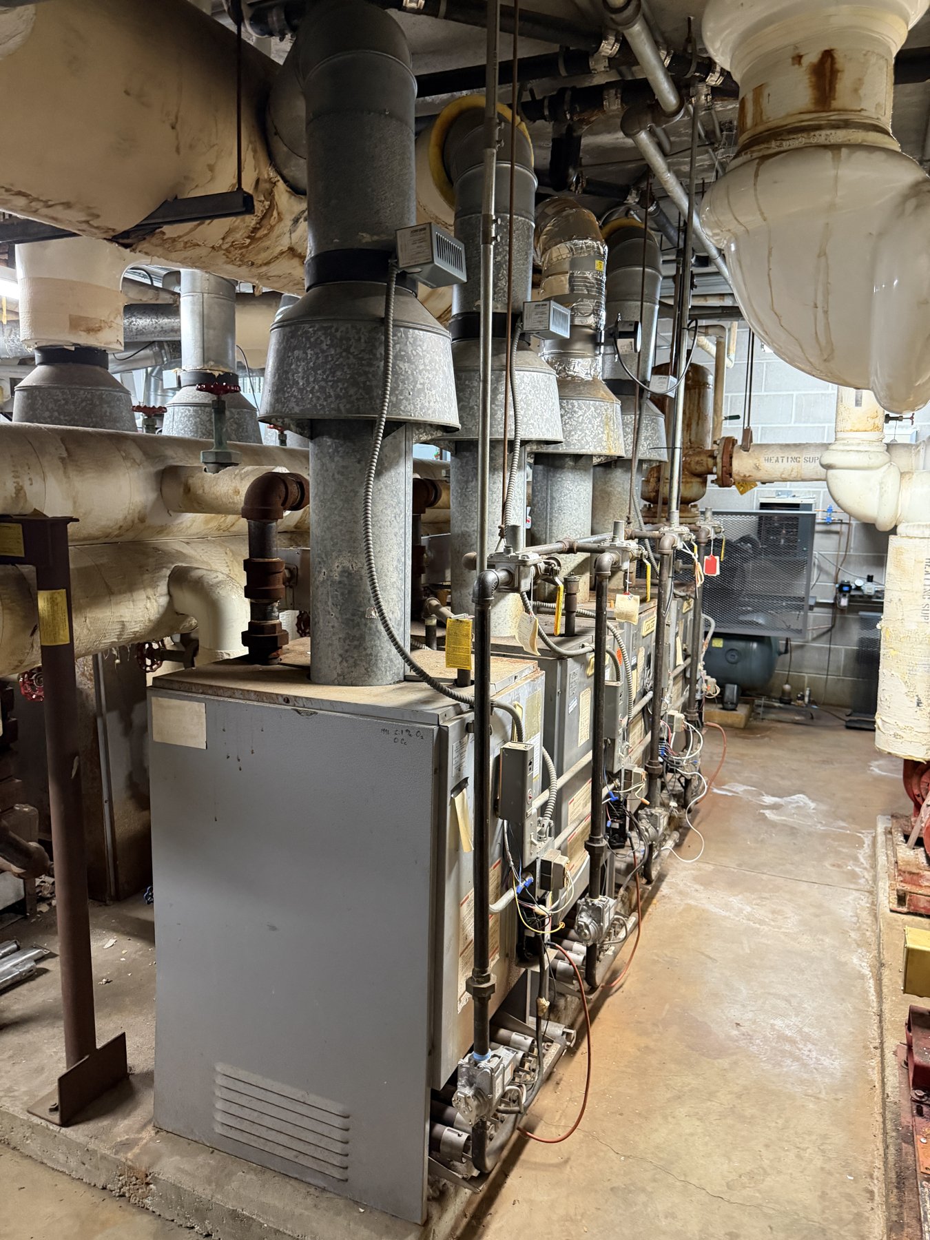 A row of commercial boilers with insulated piping in a building mechanical room