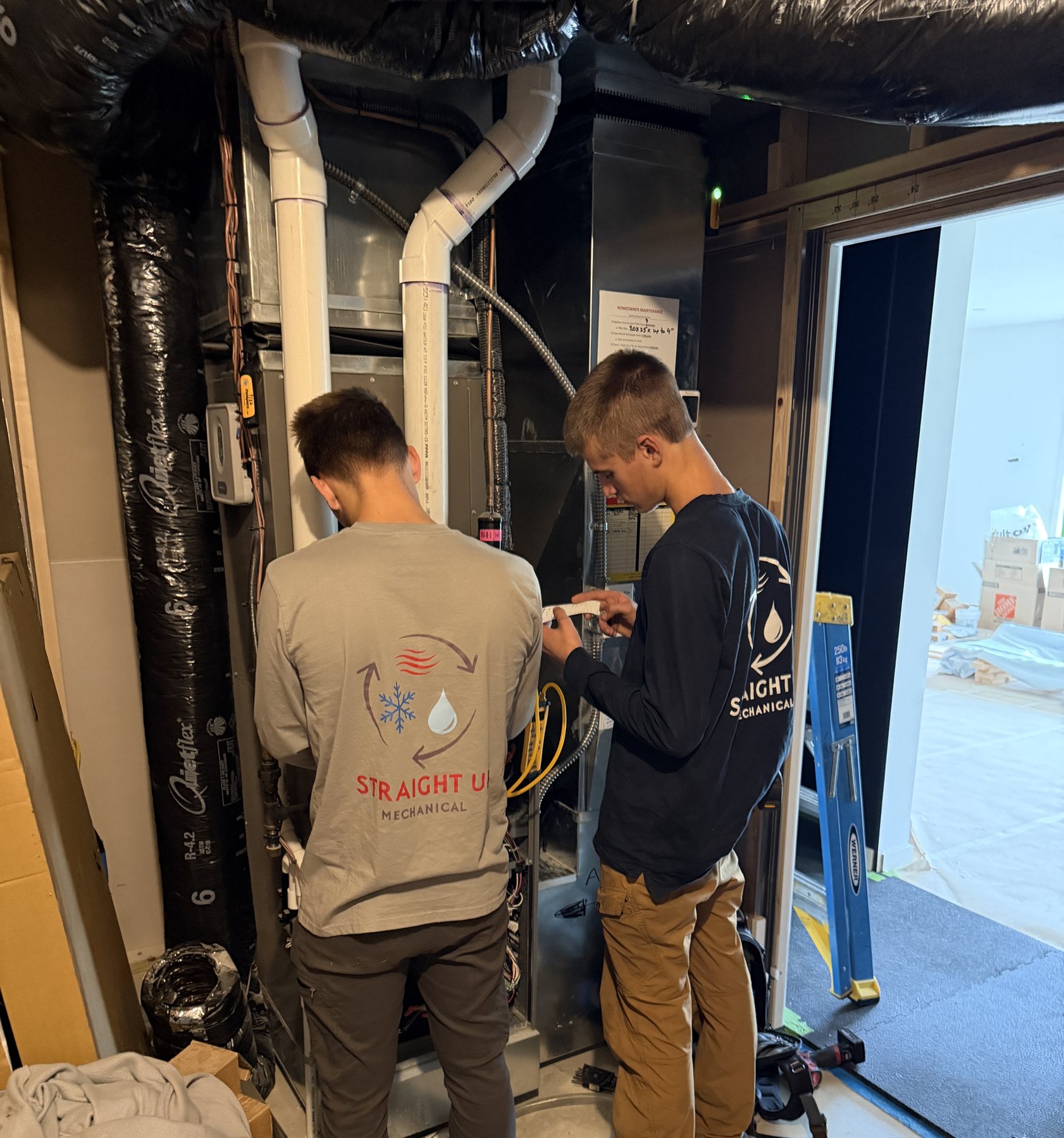 Two Straight Up Mechanical technicians working on a furnace in a residential utility room