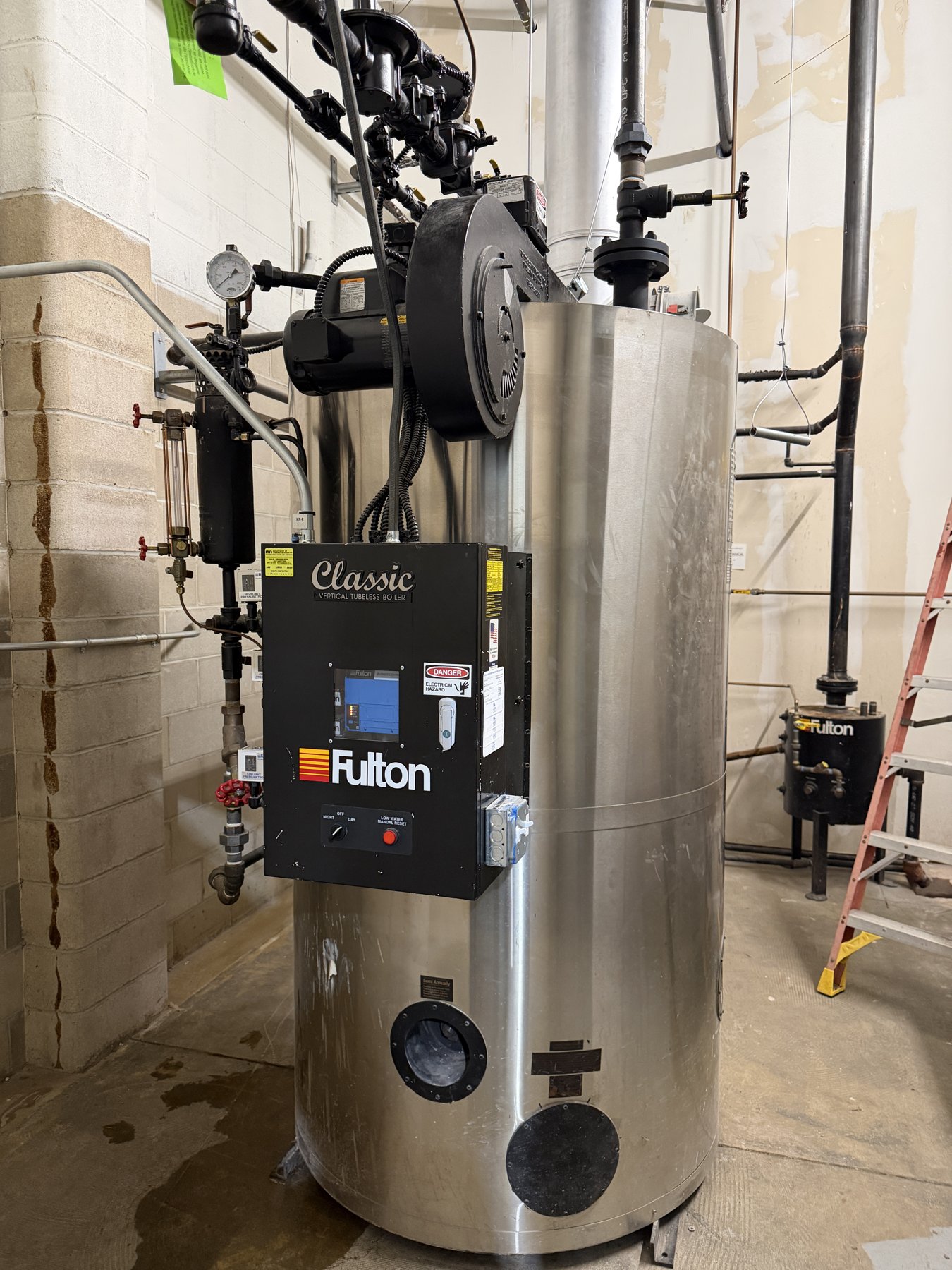 A stainless steel Fulton steam boiler with its control panel in a mechanical room