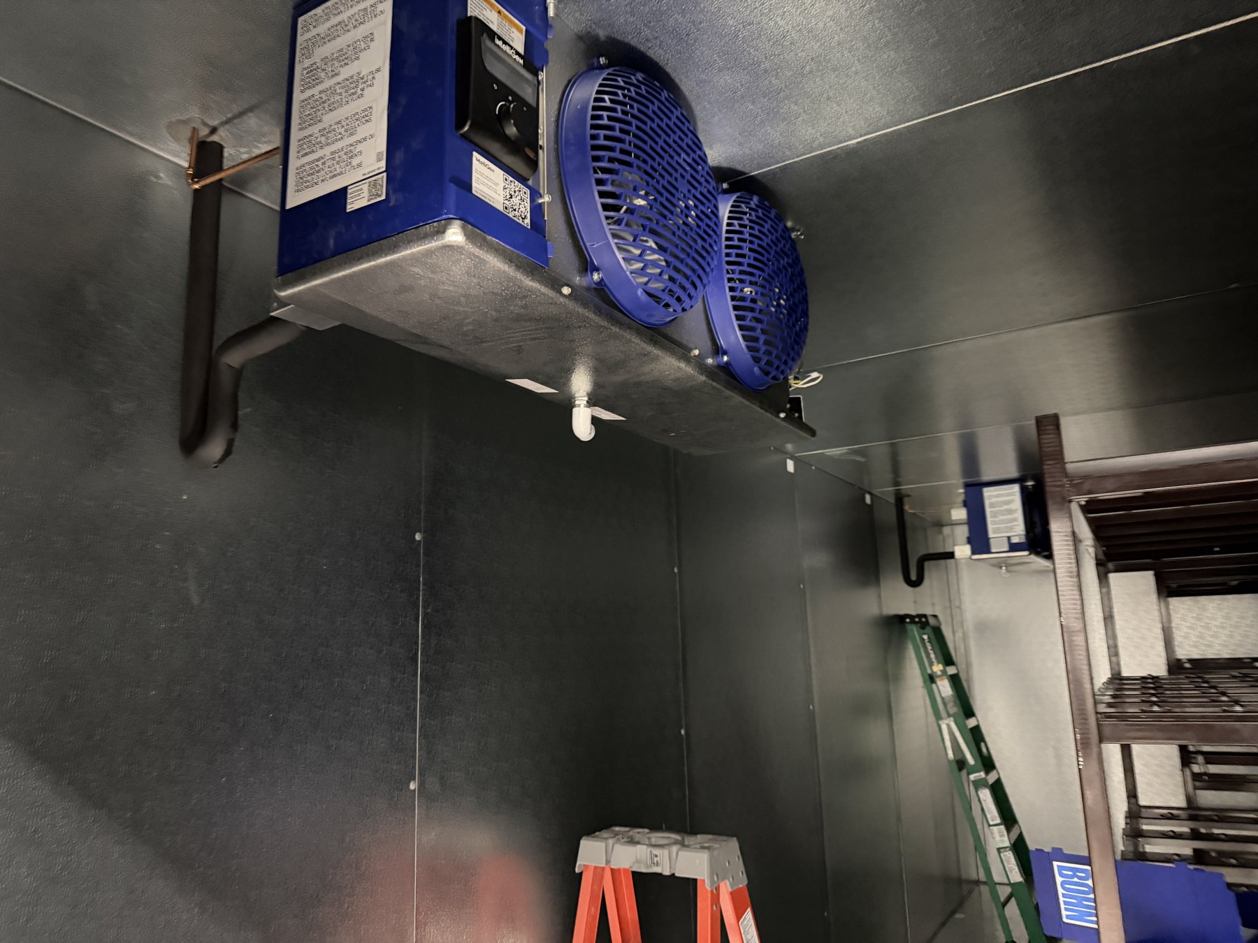 The evaporator unit and fans mounted on the ceiling inside a walk-in cooler