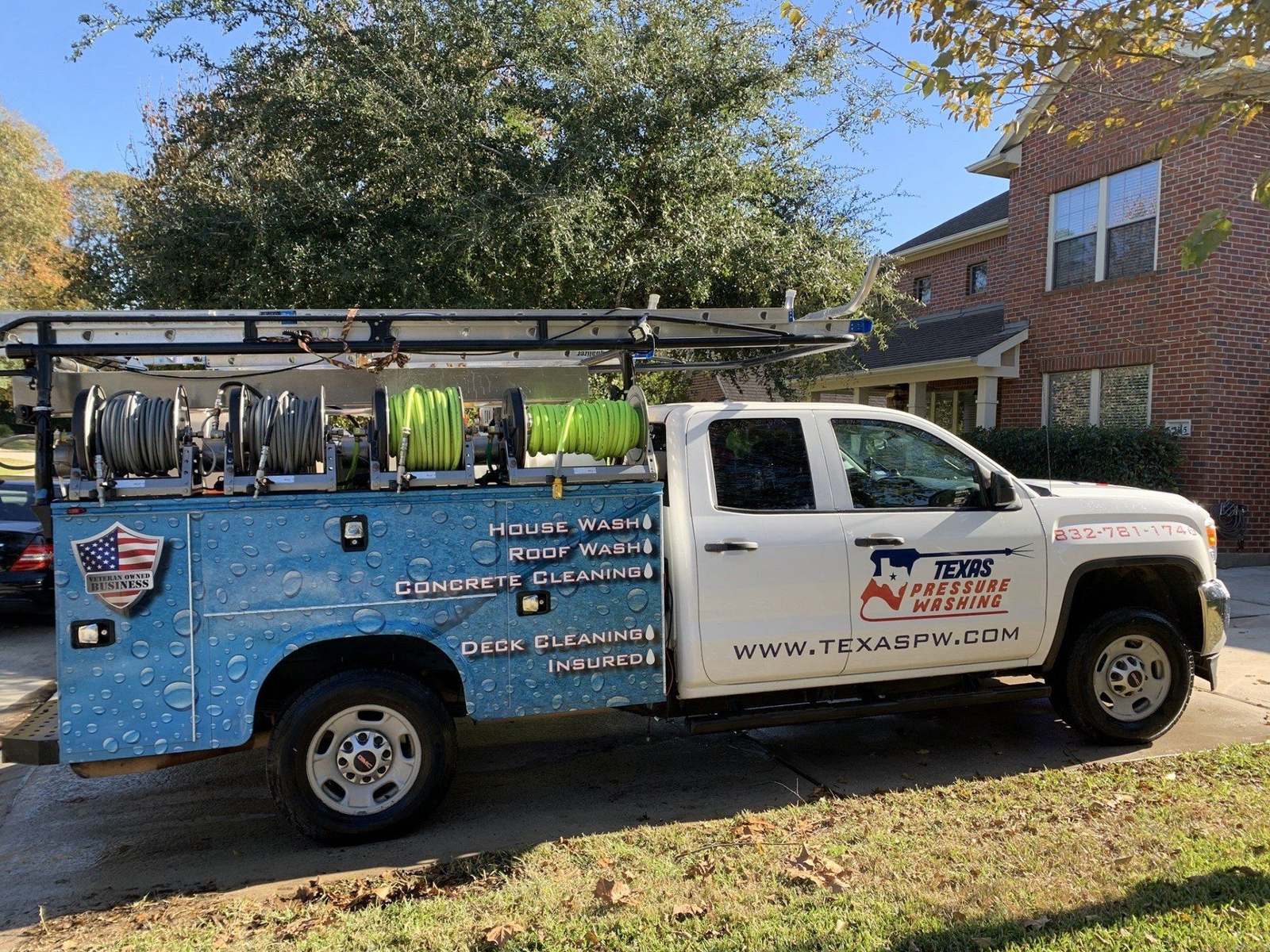 White Texas Pressure Washing service truck with hose reels and a water-droplet blue utility body parked in front of a brick house