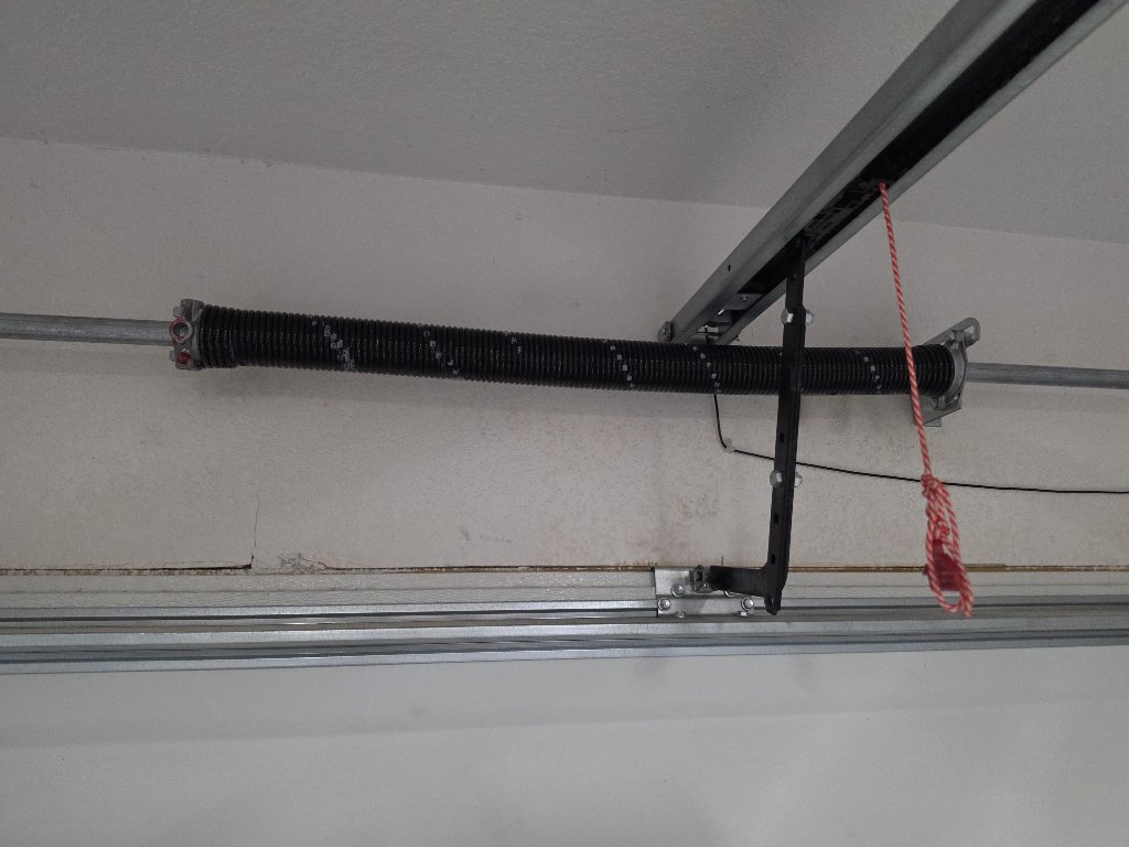 Black torsion spring mounted above a garage door with a red pull cord and track hardware