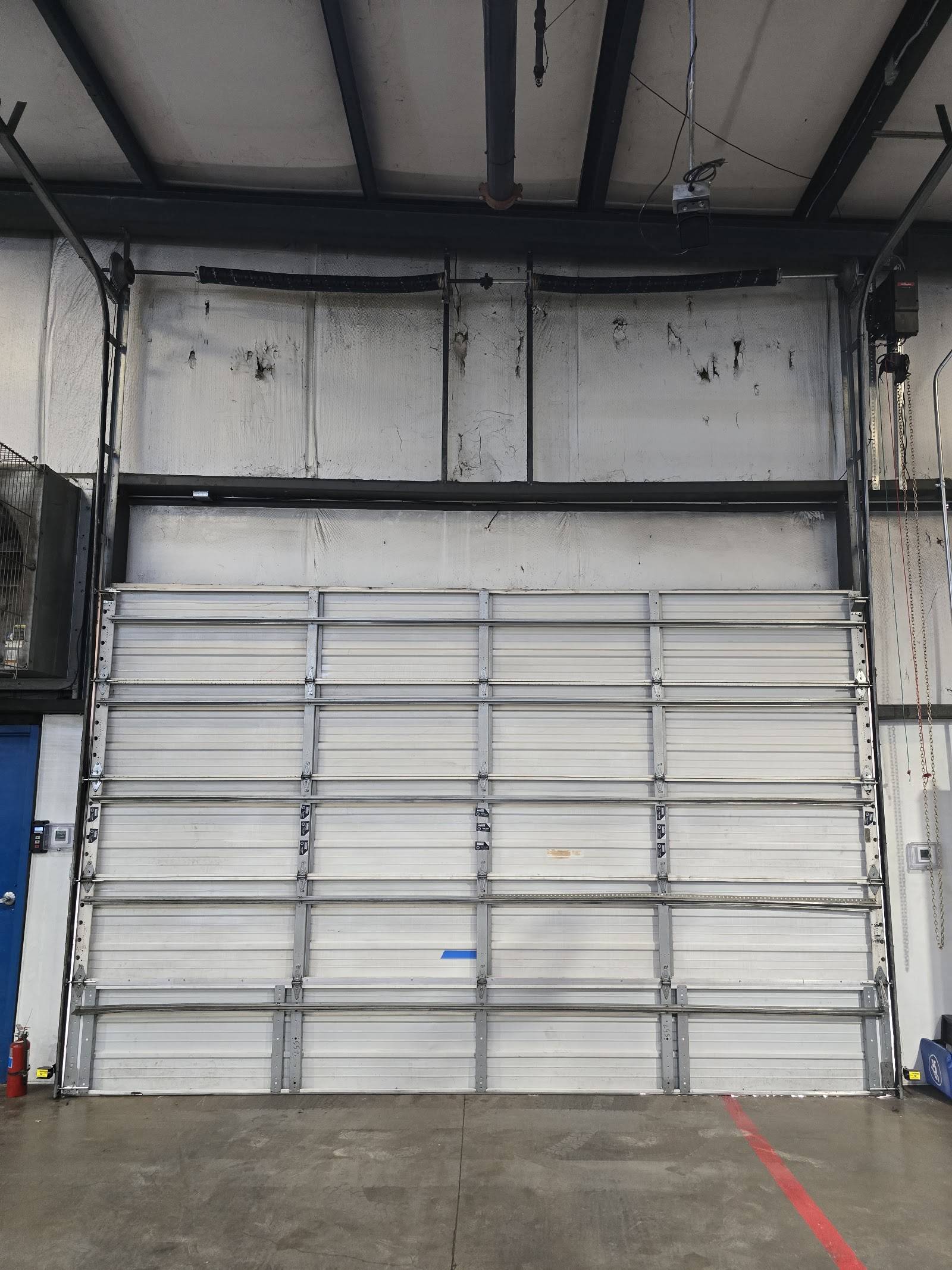 Tall white commercial overhead door inside a warehouse with springs mounted high above the opening