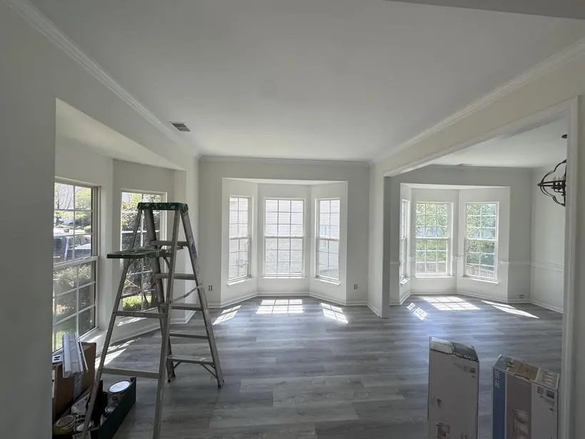 Empty bay-windowed rooms with fresh white walls and trim, a stepladder and paint supplies on the floor