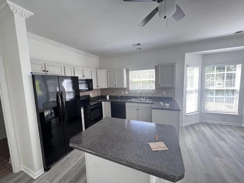 Kitchen with white painted cabinets, dark countertops, black appliances, central island and crown molding