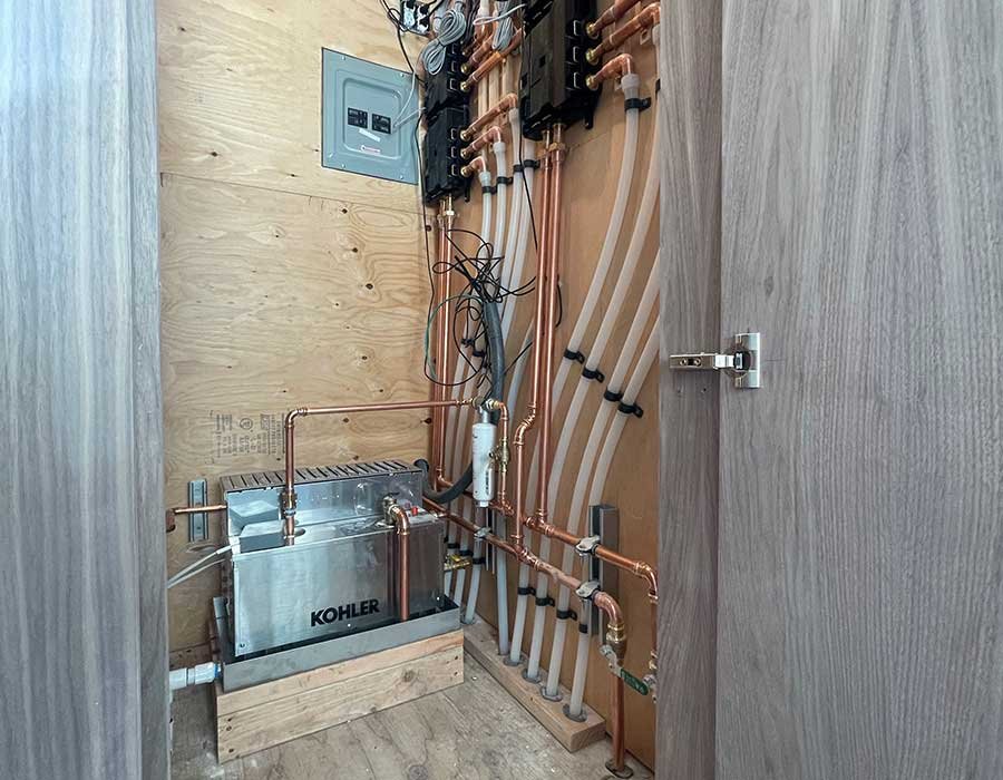 Utility closet with a Kohler steam generator and rows of copper and white supply lines mounted on a plywood wall