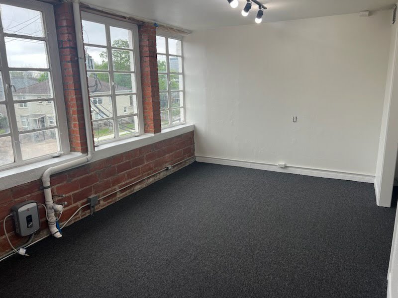 Dark carpet in an empty room with brick walls and tall windows
