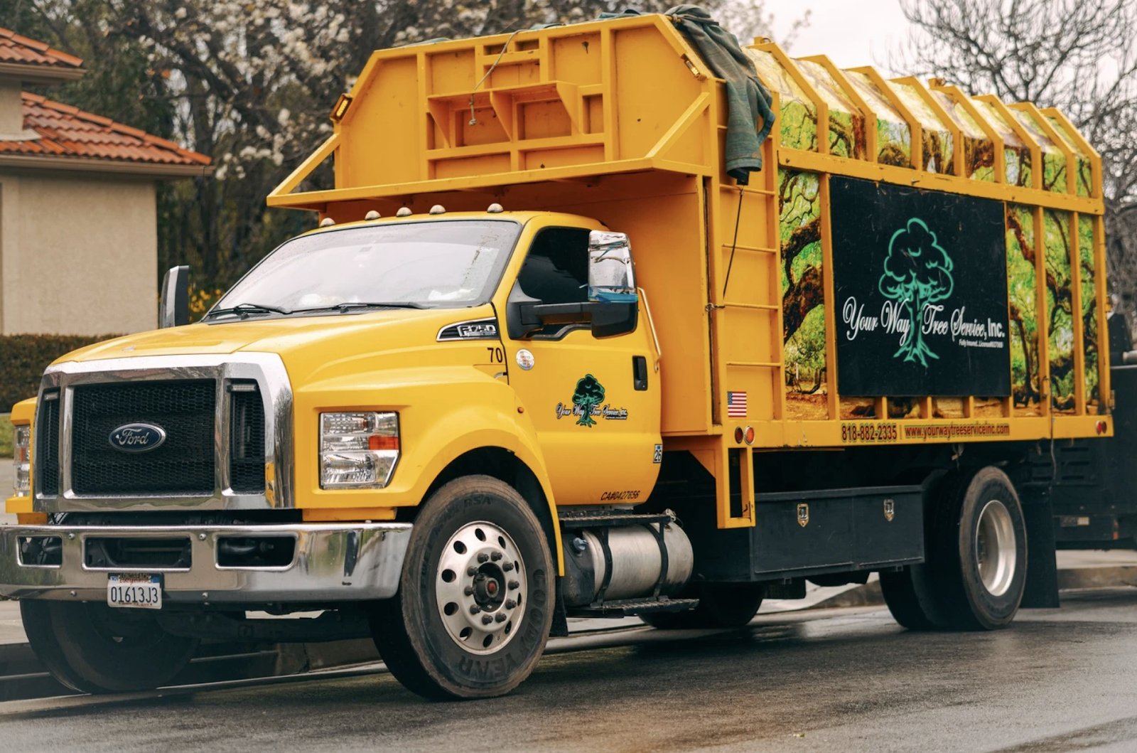 A yellow Your Way Tree Service chip truck with the company's tree logo on its box, parked on a wet residential street