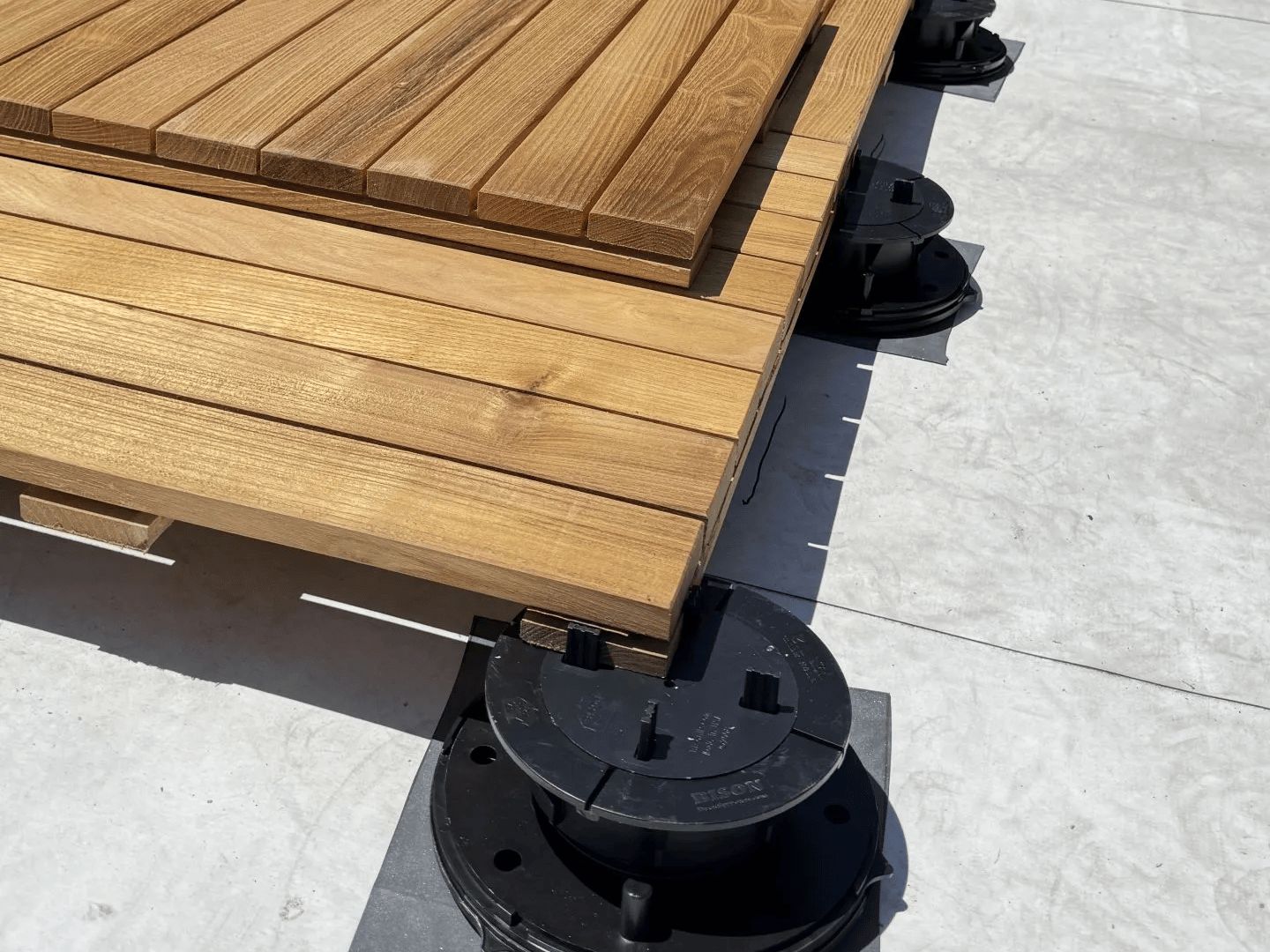 Wood deck tiles resting on black adjustable Bison pedestals over a gray rooftop membrane