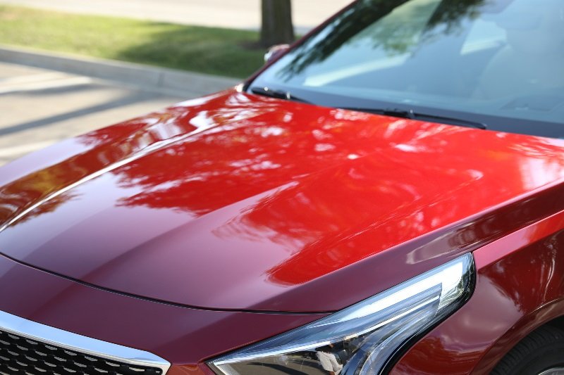 Glossy red car hood and headlight reflecting trees, showing a clean, polished paint finish
